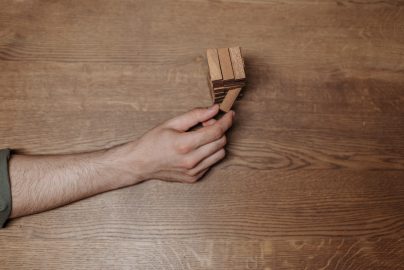 Hand zieht Holzbaustein aus Holzbausteinturm heraus